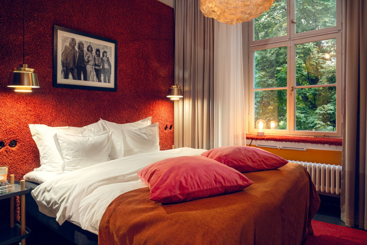 A double bed with rusty orange walls behind and two orange cushions